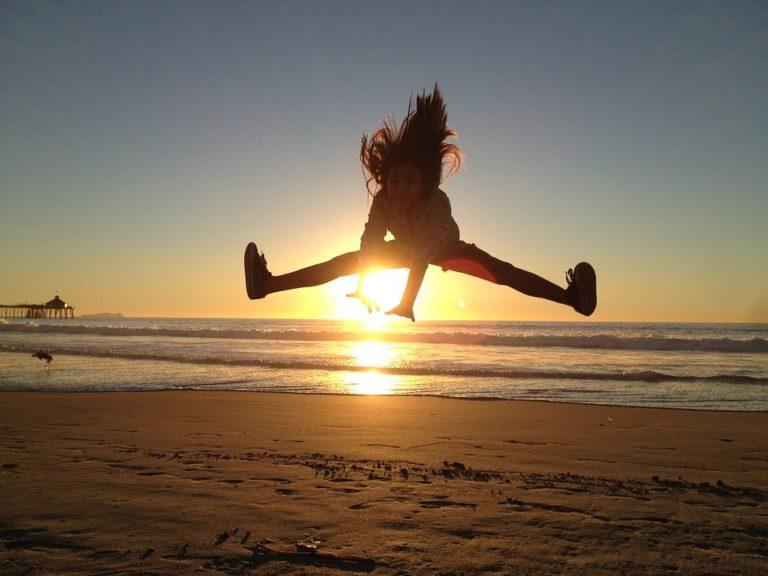 Lylusio Reiki Astrologie, sautant sur la plage devant un soleil couchant
