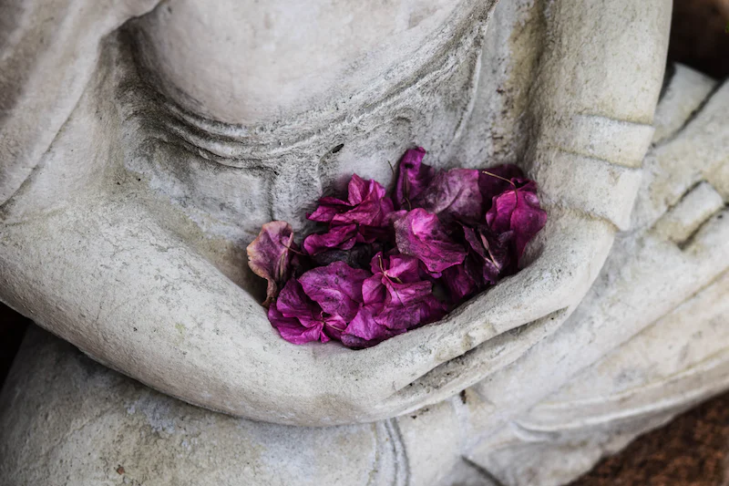 Un bouddha décoratif blanc tenant dans ses mains des pétales de fleurs
